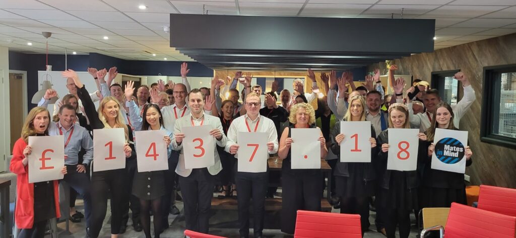 A large group of Armorgard employees with the people at the front holding up a piece of paper showing £1437.18 with each person holding up one character and the person on the end holding up a logo that says Mates in Mind