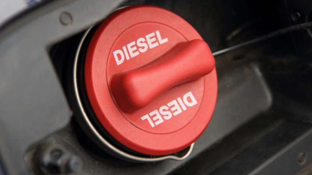 A close up of red fuel cap on a black car, the fuel cap has diesel in white writing on it