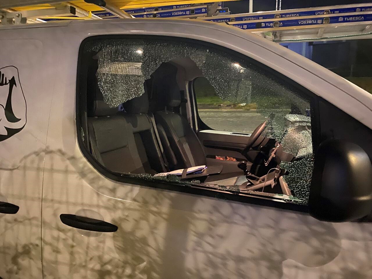 A white van with their passenger side window that has been smashed, it is a van that can be deemed to car tools for building based on the ladders on the roof of the van