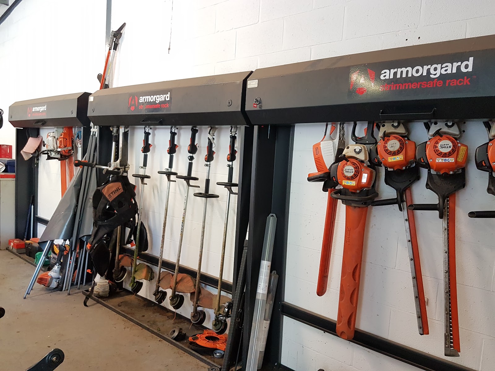 A strimmersafe rack is shown with various strimmers and long handled equipment hanging down from the racks