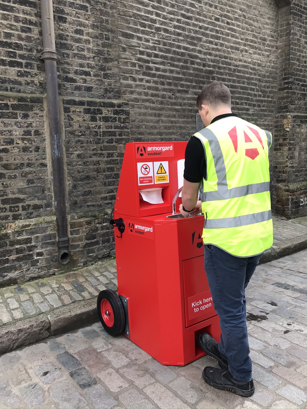 Worker using an Armorgard ScrubKart portable handwashing station on a cobblestone street
