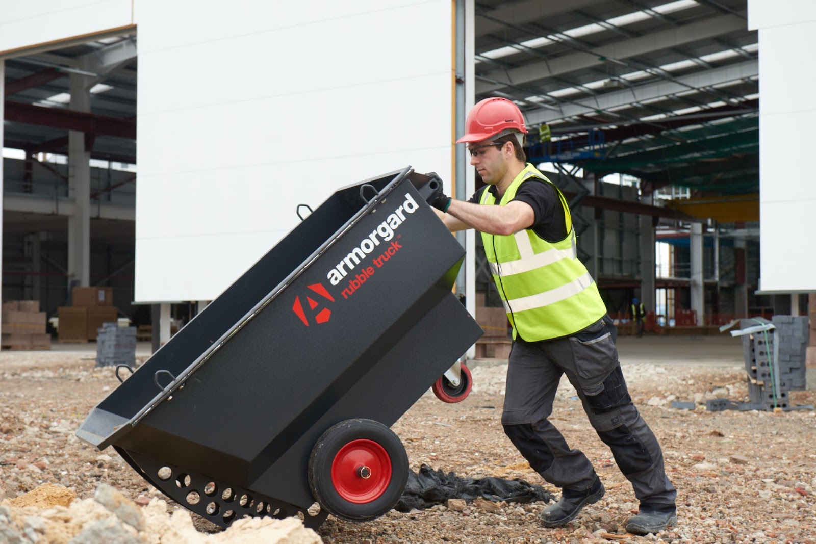 Person in a hi vis and a hard hat pushing and tipping a black RubbleTruck with Armorgard branding on it