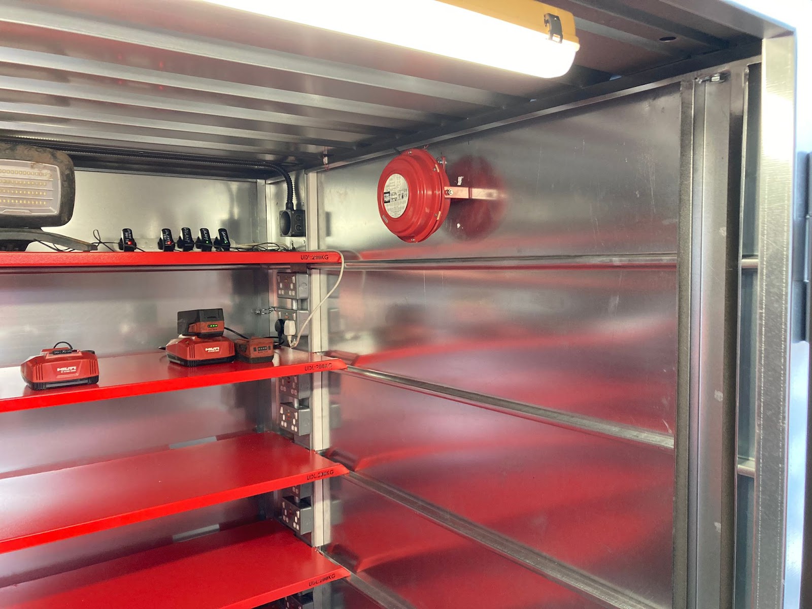 A red fire suppressant system attached to one of the walls high up just underneath the ceiling inside an Armorgard storage container, some shelves to the left of it can also be seen