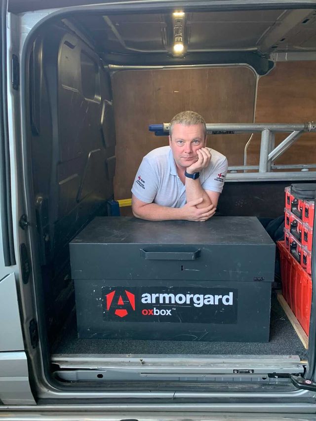 An OxBox tool chest in the van and a person kneeling down and resting his elbows on the oxbox looking at the camera