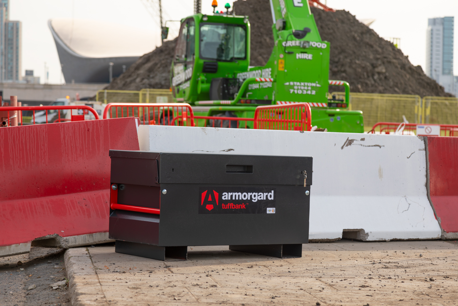 A black Tuffbank which is a tool chest and it is at a building site setting in front of some barriers and some machinery and a mound of dirt
