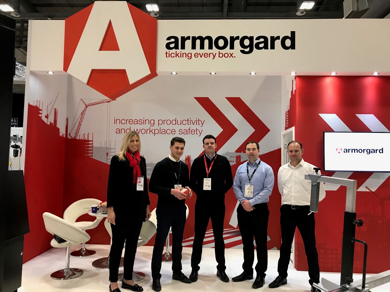 5 Staff members from Armorgard are standing in front of their red and white themed Armorgard stand at the executive hire show.