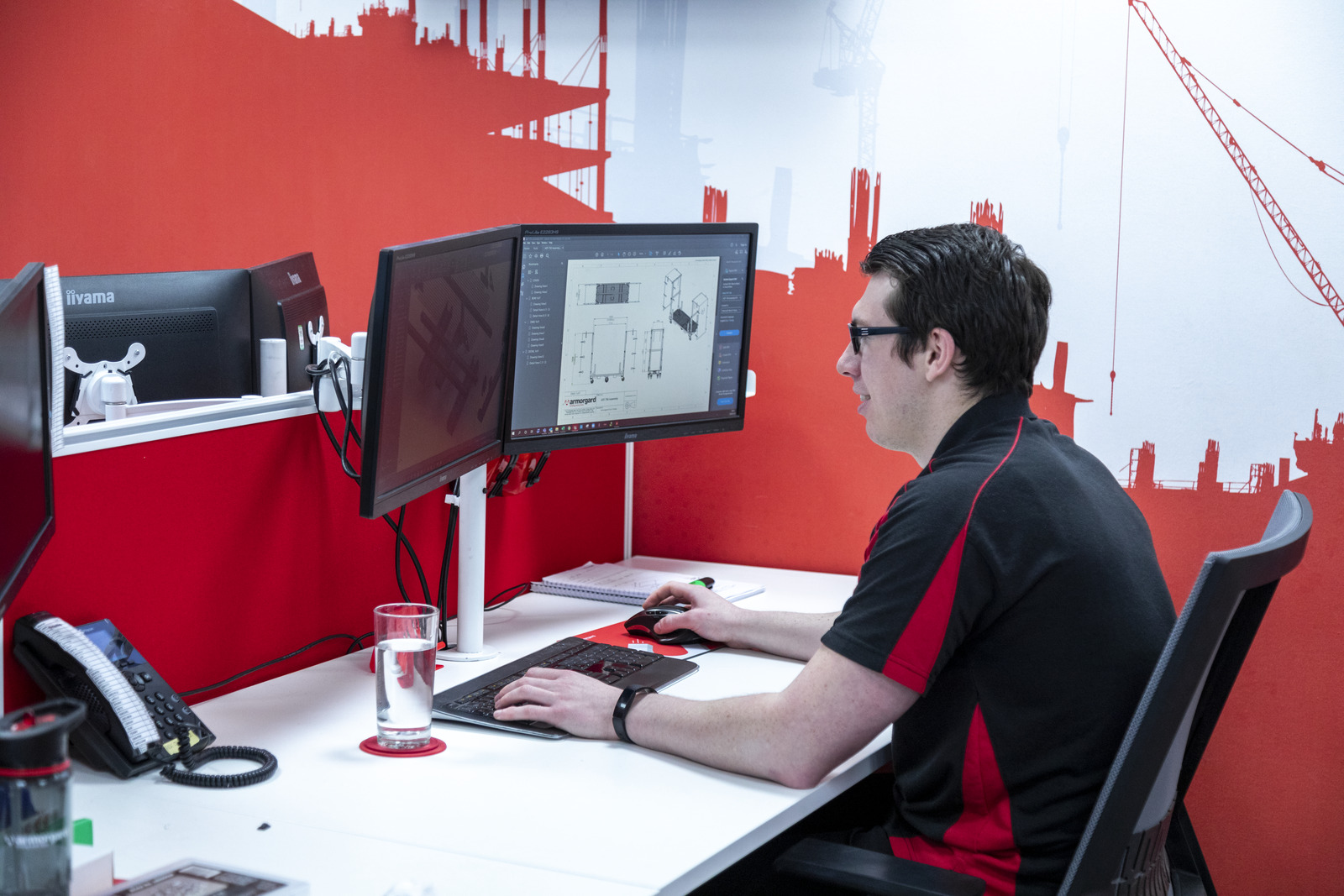 An image of an Armorgard employee sitting down working at a computer, the screen contains some designing of new products