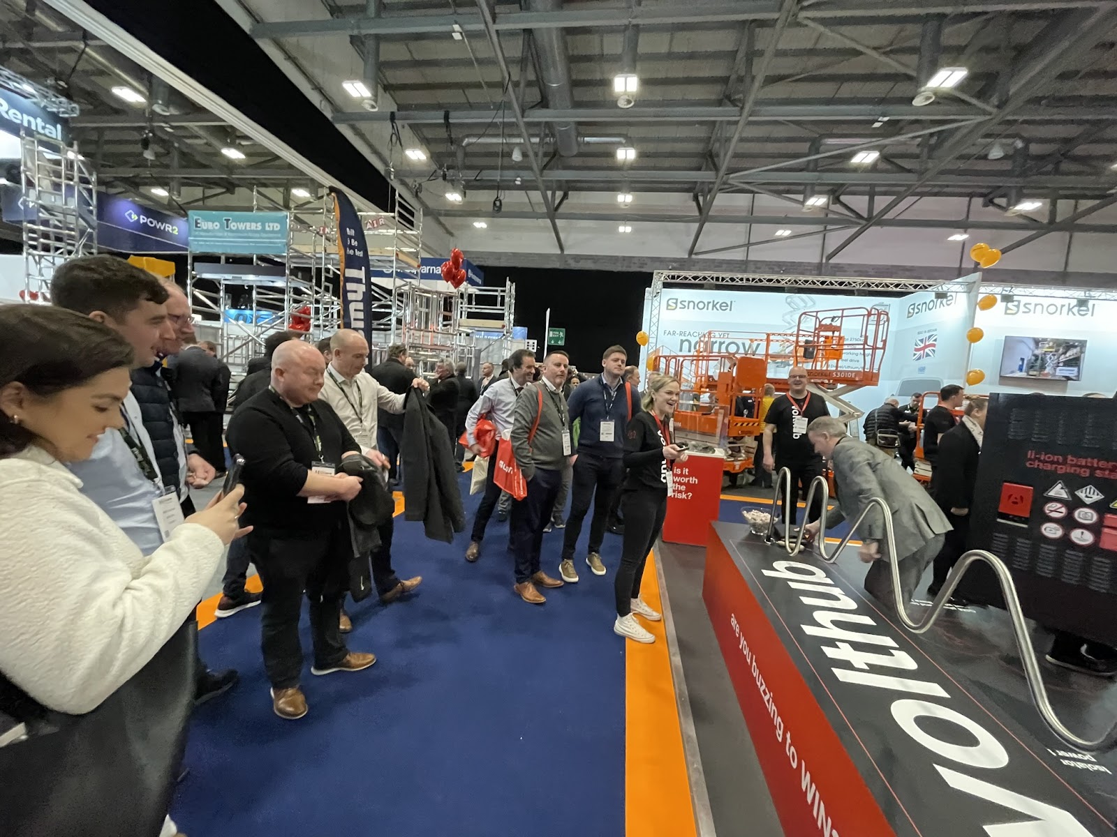 A crowd of people watching a person playing an interactive game at the Executive Hire Show