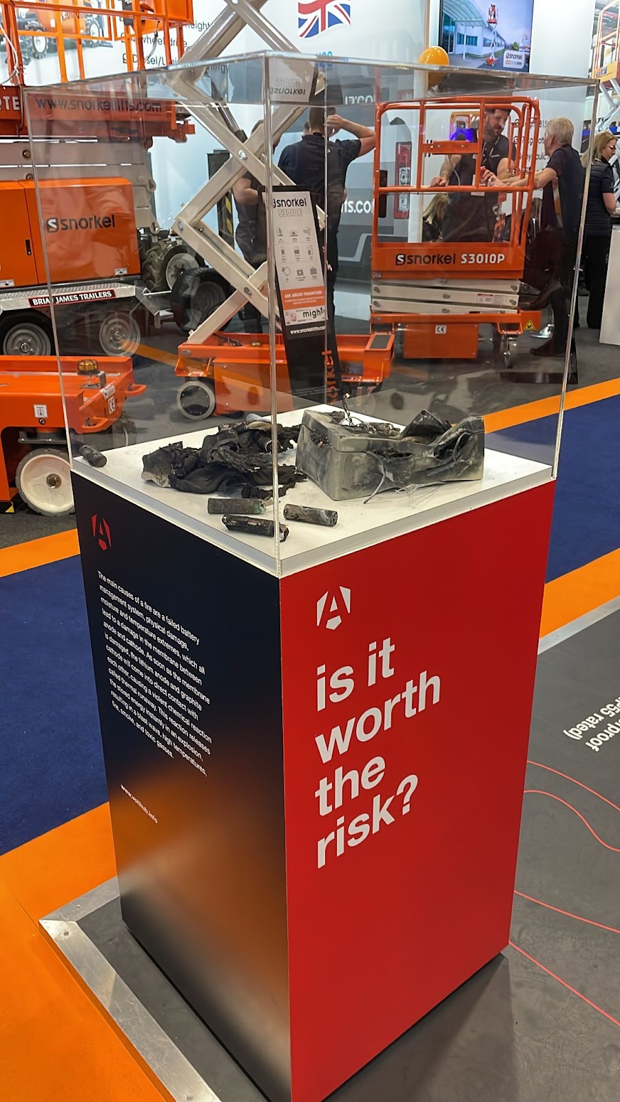 A stand saying 'is it worth the risk?' and a glass encasement showing a very damaged/burnt battery.