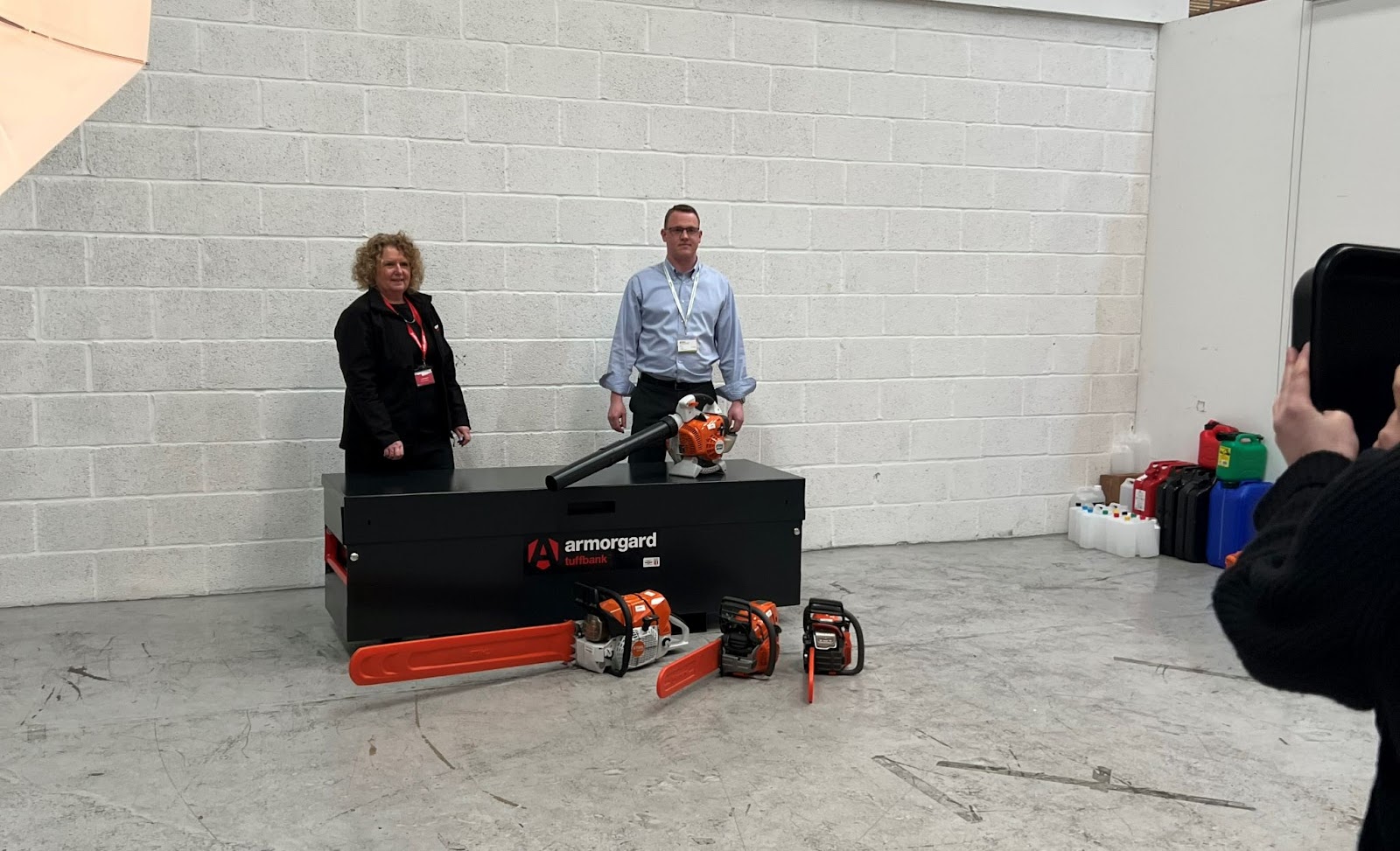 A person from Tudor Environmental and Armorgard standing behind an Armorgard storage container with 3 chainsaws and a leaf blower.
