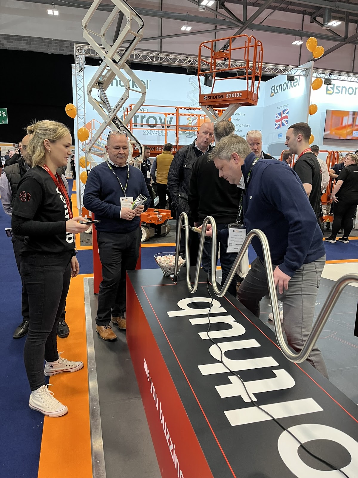 A person playing a buzz wire game at the armorgard stand at executive hire show, with a crowd of people in the background