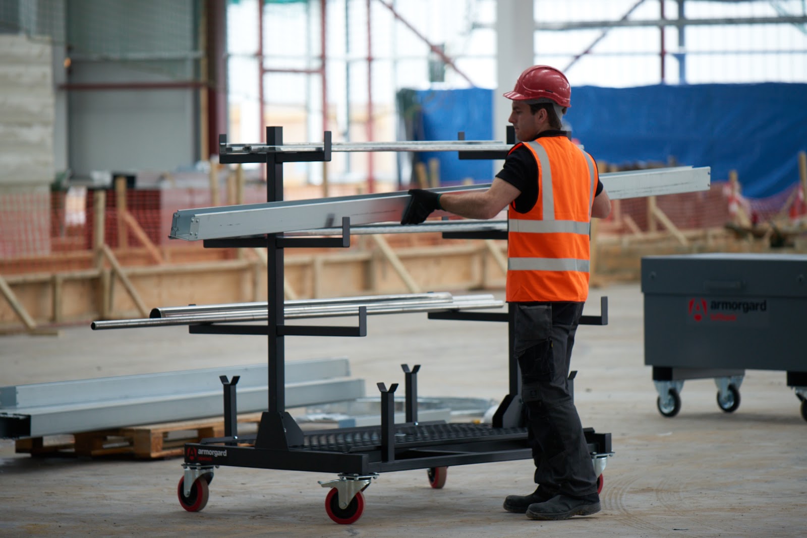 A person in an orange hi vis vest and a red hard hat putting metal rails onto an Armorgard PipeRack