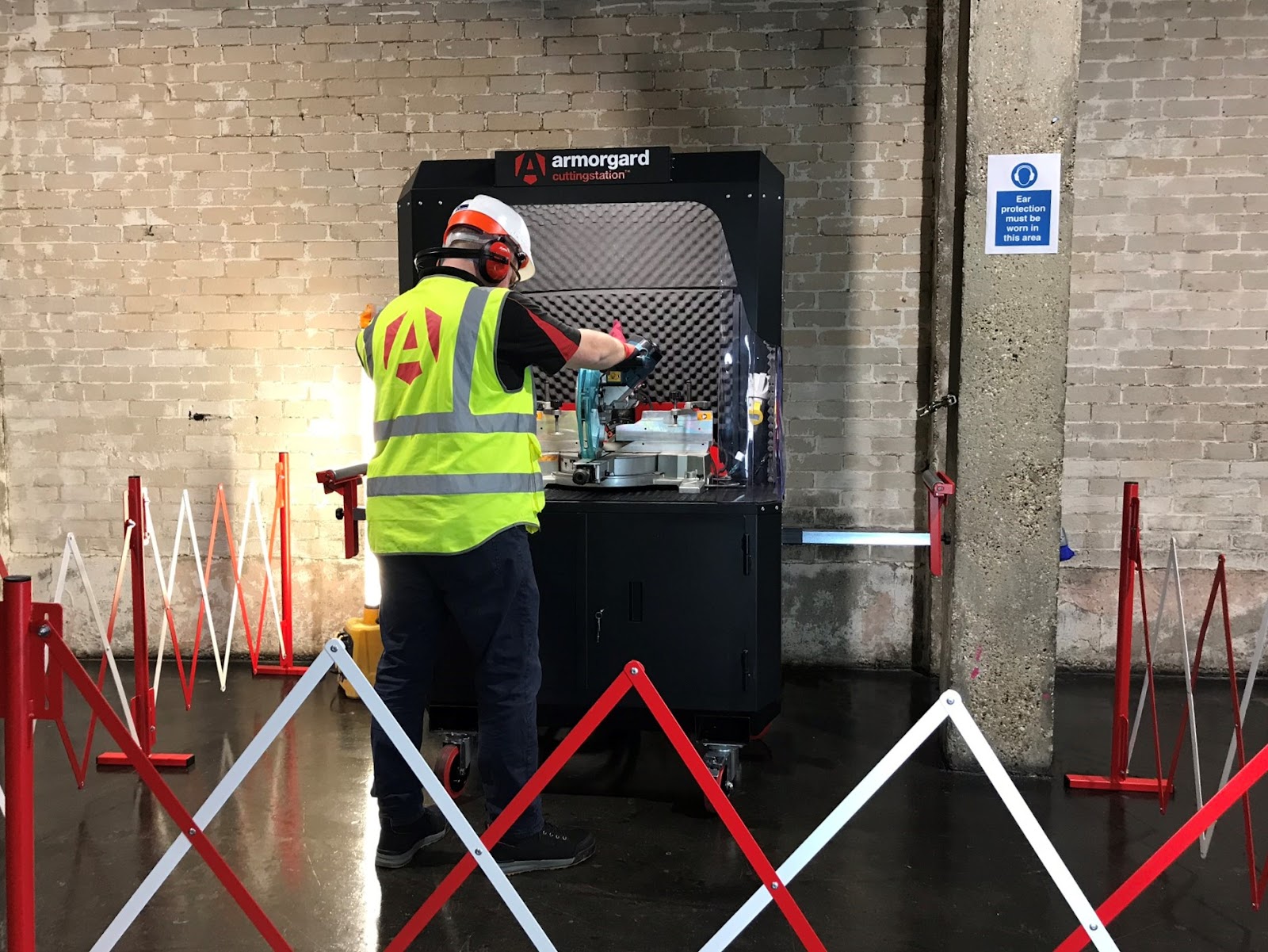 A person in a hi vis, helmet and ear protection using the armorgard cutting station to cut some materials with in a cordoned of area